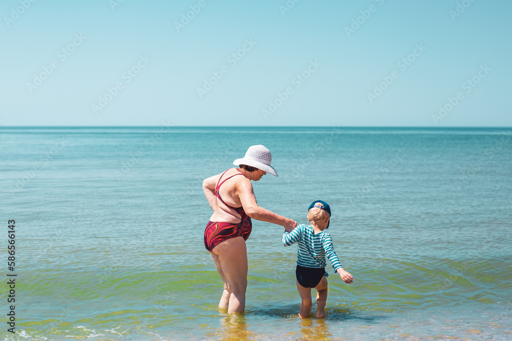 Grandmother and grandson go into the sea for swimming. Summer holidays on the sea coast with the whole family