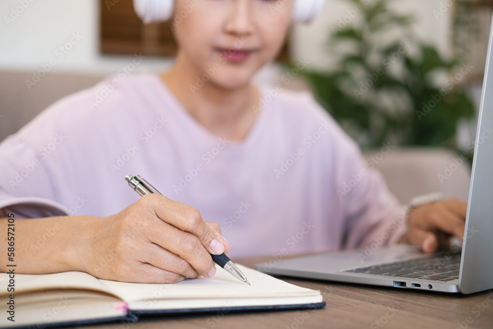 Close up hand - Attractive female student learning language, watching online webinar, listening audio course, Focused woman wearing headphones using laptop writing notes, e-learning education concept Close up hand - Attractive female student learning language, watching online webinar, listening audio course, Focused woman wearing headphones using laptop writing notes, e-learning education concept