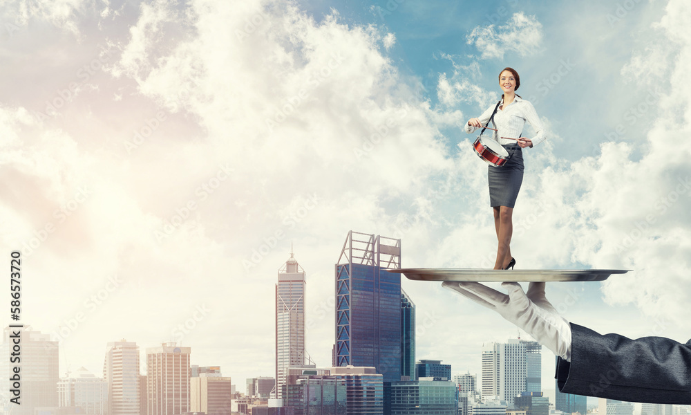 Attractive businesswoman on metal tray playing drums against cityscape background Attractive businesswoman on metal tray playing drums against cityscape background