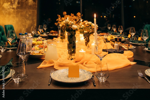 Luxury table setting for a celebration in a restaurant. Dark tones of orange and green are the colors of the holiday. Tableware and catering for the holiday