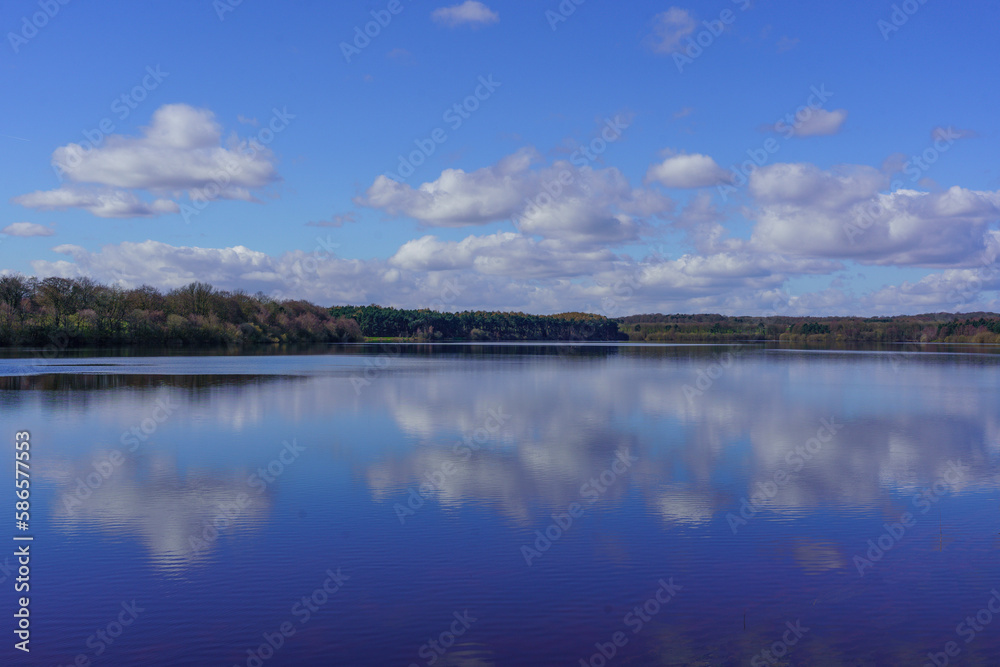 A calm sunny day with a view across Eccup Reservoir creating stunning reflections of blue sky and white clouds, Leeds, England, West Yorkshire, UK. 