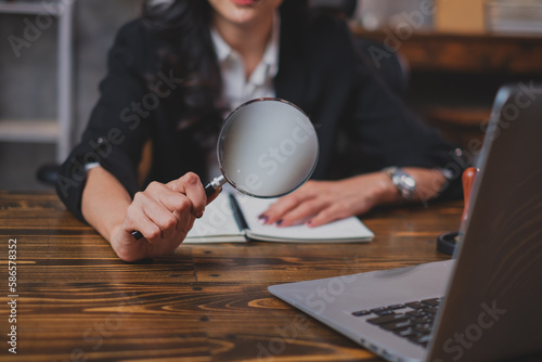 A Female manager is holding a magnifying glass. Concept of searching document, hiring employees, browsing data of company, online research, marketing inspection or analysis. Using lens to focus profit