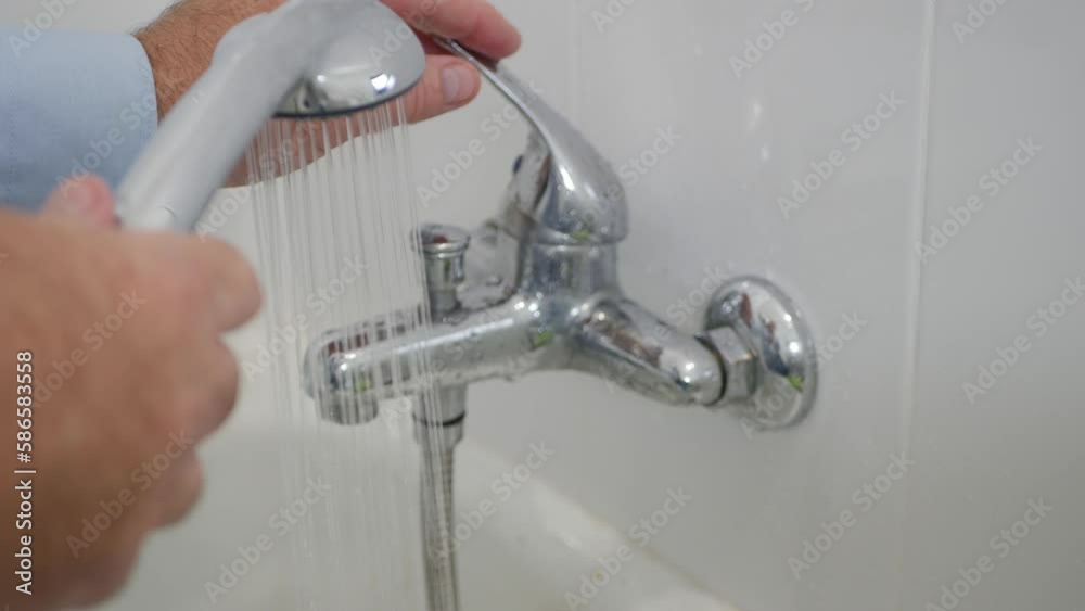 Blurred Shooting with a Person Using the Bathroom Showerhead. Man Preparing a Bath Using Hot Water from a Showerhead. Blurred Shooting with a Person Using the Bathroom Showerhead. Man Preparing a Bath Using Hot Water from a Showerhead.