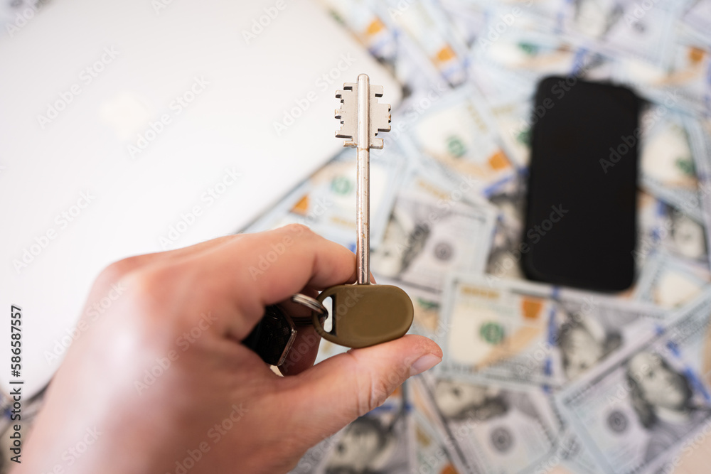 Man hand hold key on dollar money, laptop and phone background. Man hand hold key on dollar money, laptop and phone background.