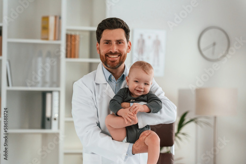 Holding boy in hands. Doctor with little baby is working in the cabinet