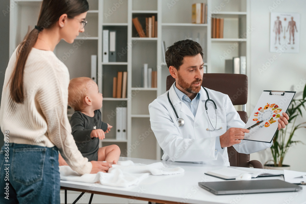 Talking about healthy eating. With baby and mother. Doctor in formal clothes is working in the cabinet Talking about healthy eating. With baby and mother. Doctor in formal clothes is working in the cabinet
