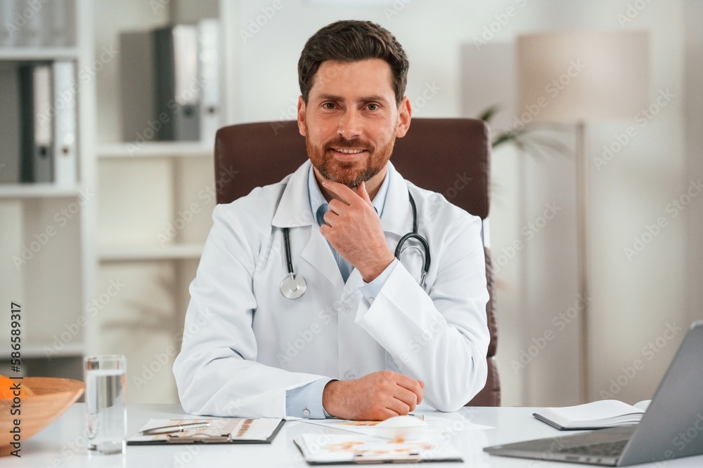In white coat, sitting. Doctor in formal clothes is working in the cabinet In white coat, sitting. Doctor in formal clothes is working in the cabinet