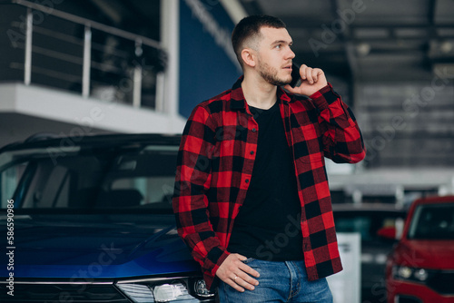 Man choosing a car in a car showroom and using phone