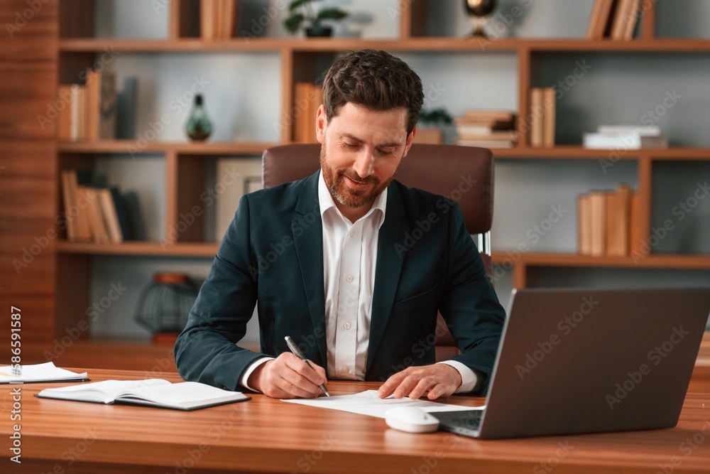 Sitting by table with laptop. Businessman in formal clothes is working indoors Sitting by table with laptop. Businessman in formal clothes is working indoors