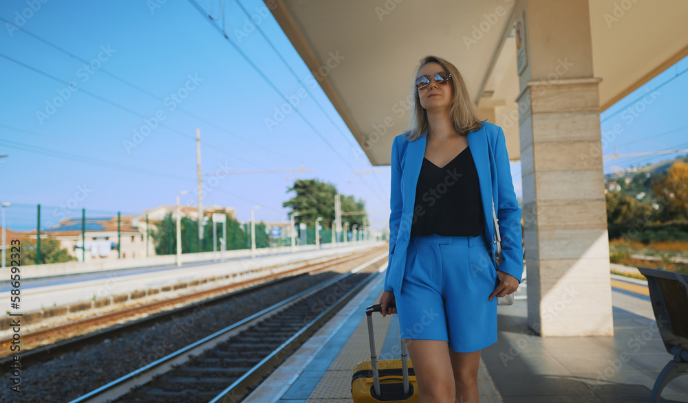 Woman with a suitcase walks along the platform at the train station.