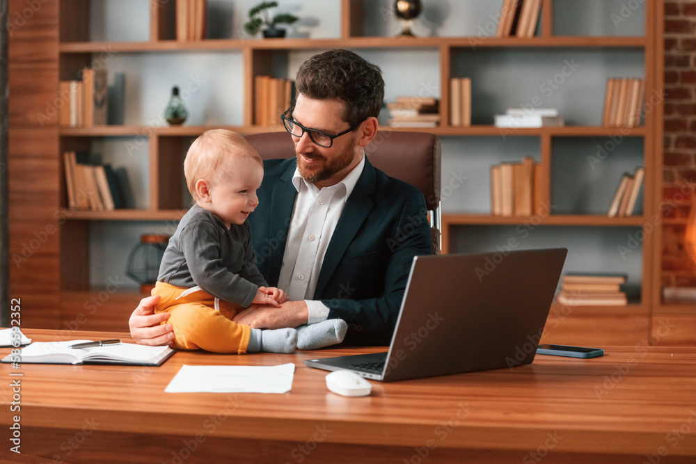 With toddler. Businessman in formal clothes is working indoors With toddler. Businessman in formal clothes is working indoors