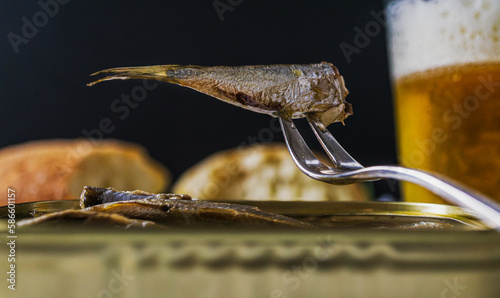 Canned sardine on a small fork. Glass of beer in the background.
