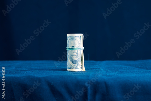 100 bills rolled up into a tube and tied with a rubber band on a blue background Franklin has a rubber band covering his eyes. Symbol of bribery, unscrupulousness of income, concealment of tax income photo