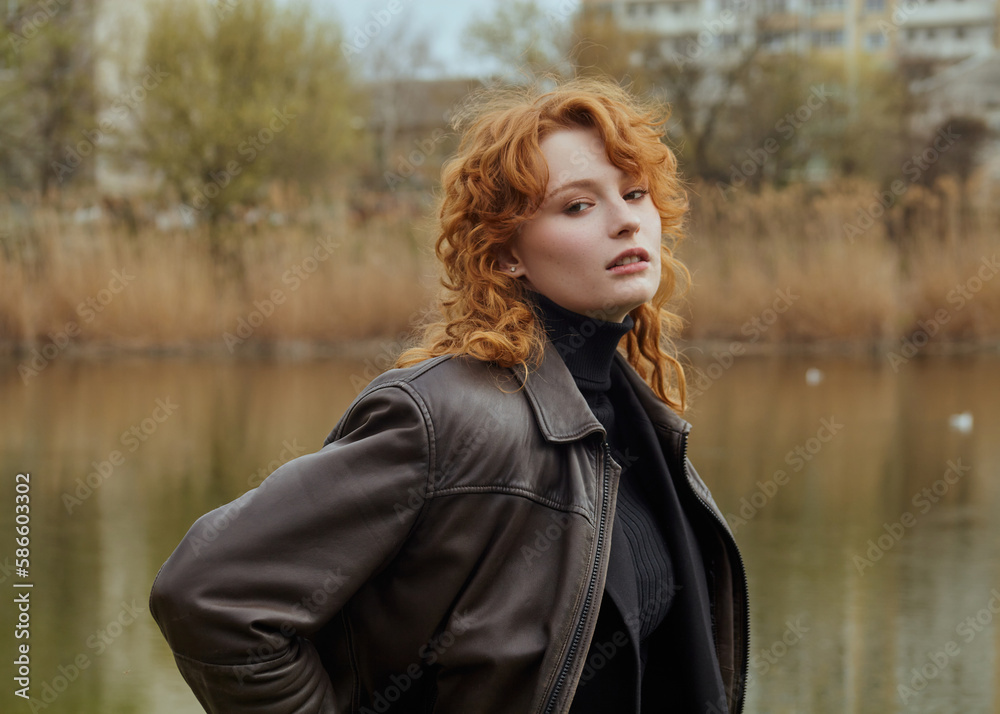 a beautiful red-haired woman walks in the park near the lake in a leather jacket, enjoying a pleasant day a beautiful red-haired woman walks in the park near the lake in a leather jacket, enjoying a pleasant day