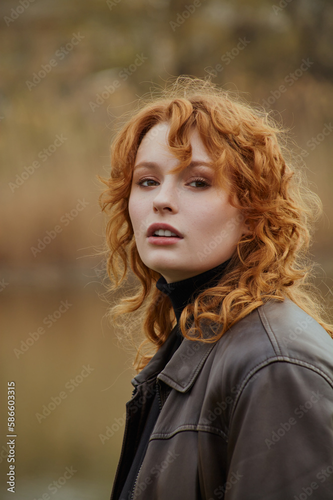 a beautiful red-haired woman walks in the park near the lake in a leather jacket, enjoying a pleasant day a beautiful red-haired woman walks in the park near the lake in a leather jacket, enjoying a pleasant day