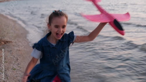 Little happy girl runs with a toy airplane across the field in the park. A young girl plays with a toy plane and dreams. The girl wants to become a pilot and an astronaut. Dreamer airplane pilot. High
