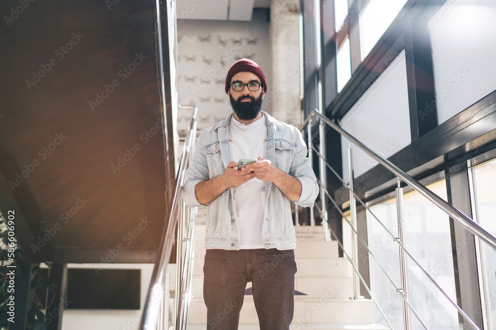 Young hipster browsing mobile phone standing on stairway