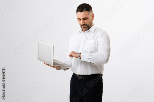 Business career and time management. Middle aged businessman using laptop and checking time, grey background