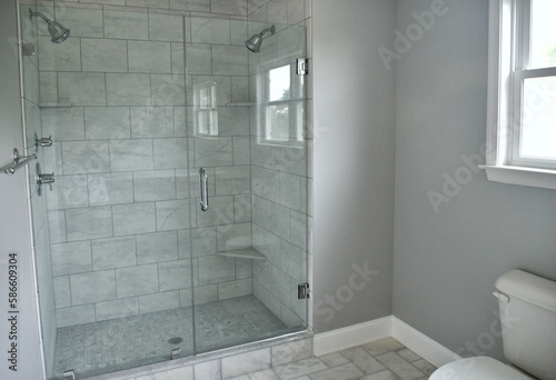 Shower with two shower heads and glass doors, gray tiles for sleek modern look.