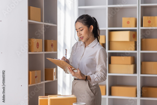 Confident young Asian woman retail sme seller, entrepreneur, online store drop shipping small business owner work of delivery SME shipping warehouse with parcel boxes.