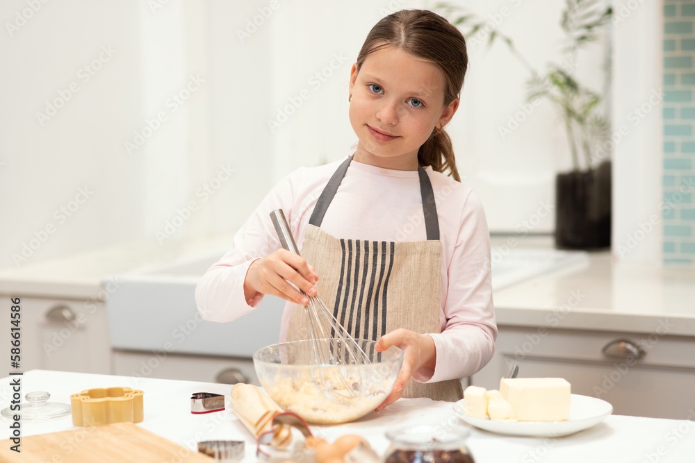 Cheerful caucasian little girl in apron make cookie dough with whisk in kitchen interior, copy space Cheerful caucasian little girl in apron make cookie dough with whisk in kitchen interior, copy space