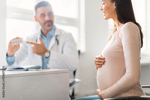 Pregnancy and medicine concept. Male gynecologist giving pills to pregnant lady during appointment at hospital
