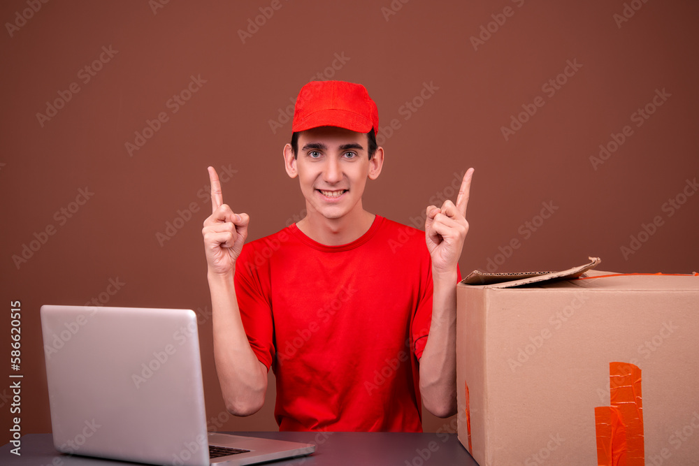 Funny courier in a red uniform sits at his desk. Brown background. Funny courier in a red uniform sits at his desk. Brown background.