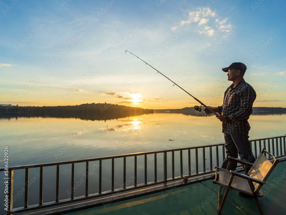 Man enjoys catching fish in the river on the background orange sunset.