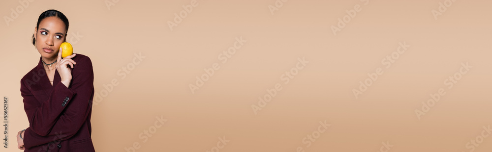 african american woman in burgundy blazer holding ripe lemon on beige background, banner. african american woman in burgundy blazer holding ripe lemon on beige background, banner.