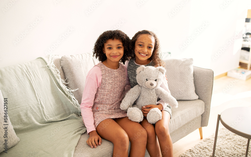 Two Cute African American Sisters Hugging Sitting On Sofa Indoors Two Cute African American Sisters Hugging Sitting On Sofa Indoors