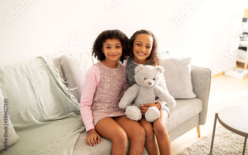 Two Cute African American Sisters Hugging Sitting On Sofa Indoors