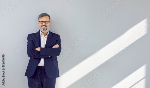 Fotografija Happy handsome mature businessman in a dark blue suit leaning against the gray wall of his office