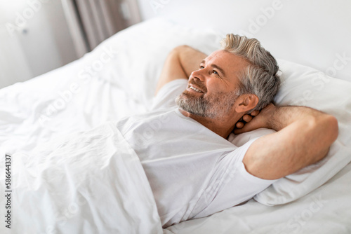 Well-rested happy middle aged man relaxing in bed
