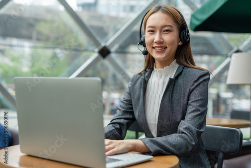 Young asian businesswoman working on her computer laptop and headset microphone in a cafe. Customer service executive working out of home. Hybrid workplace.