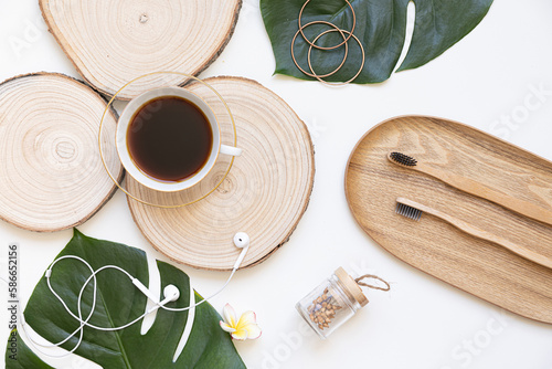 Bamboo toothbrush and coffee on a table with copy space on a white background. Styled composition of flat lay with tropical leaves.