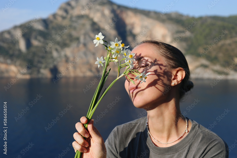 Portrait of a young woman on a cliff over the sea covering her face with wild daffodil flowers. Close up, copy space, background. Portrait of a young woman on a cliff over the sea covering her face with wild daffodil flowers. Close up, copy space, background.