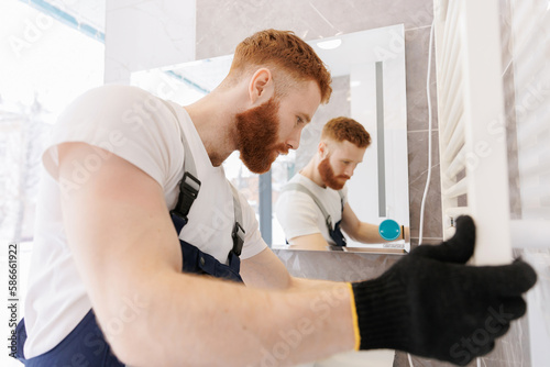 Plumber installing electric battery for towels, work in bathroom