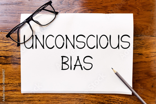 Unconscious bias text on blank notebook paper on wooden table with pencil and glasses aside. Business concept and legal concept about unconscious bias.