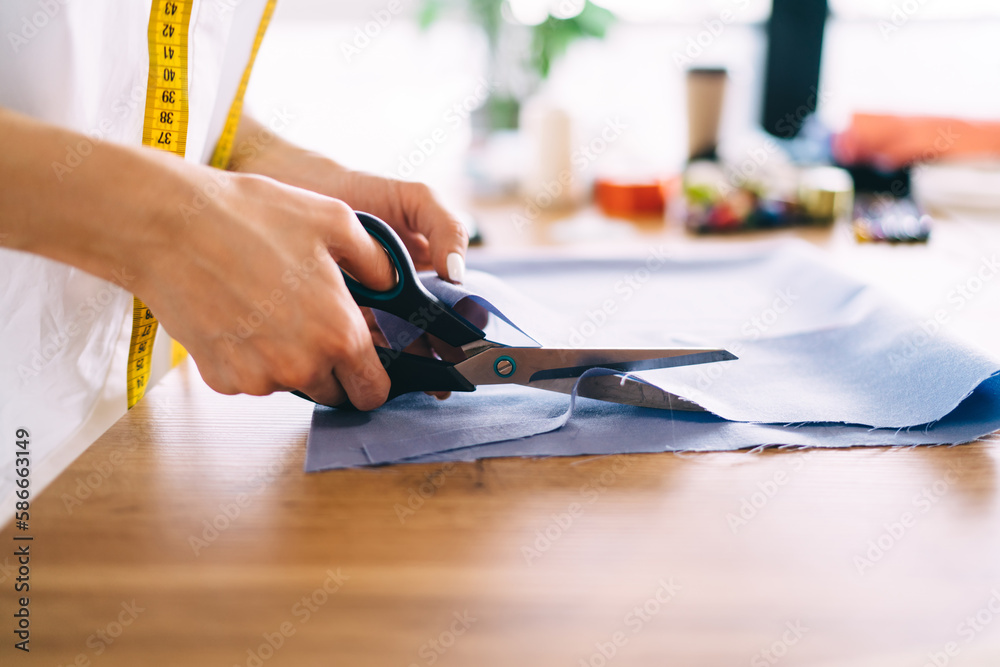 Obraz premium Crop woman cutting fabric on table in workshop