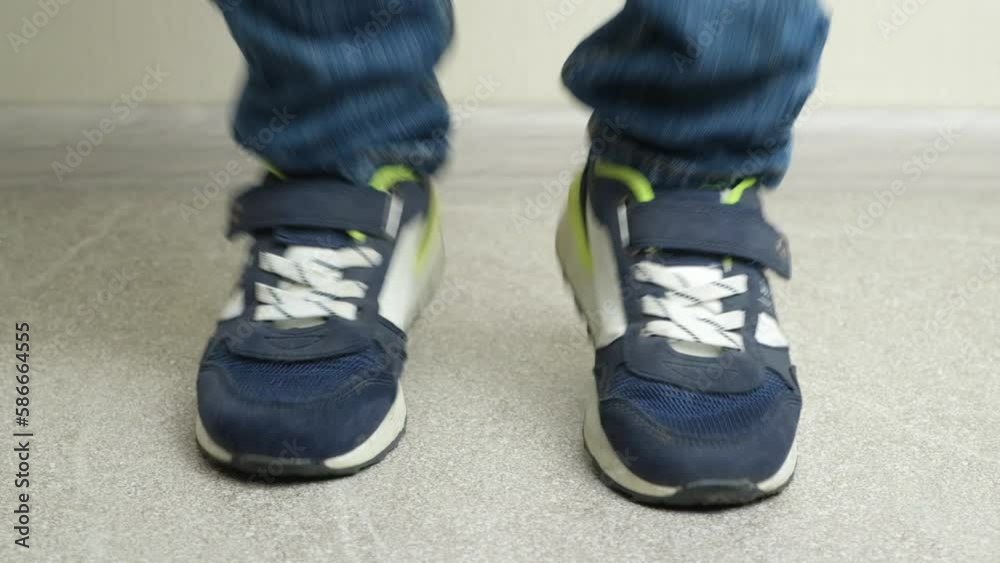 A preschool or junior school boy jumps in sneakers on the floor, close-up of his legs