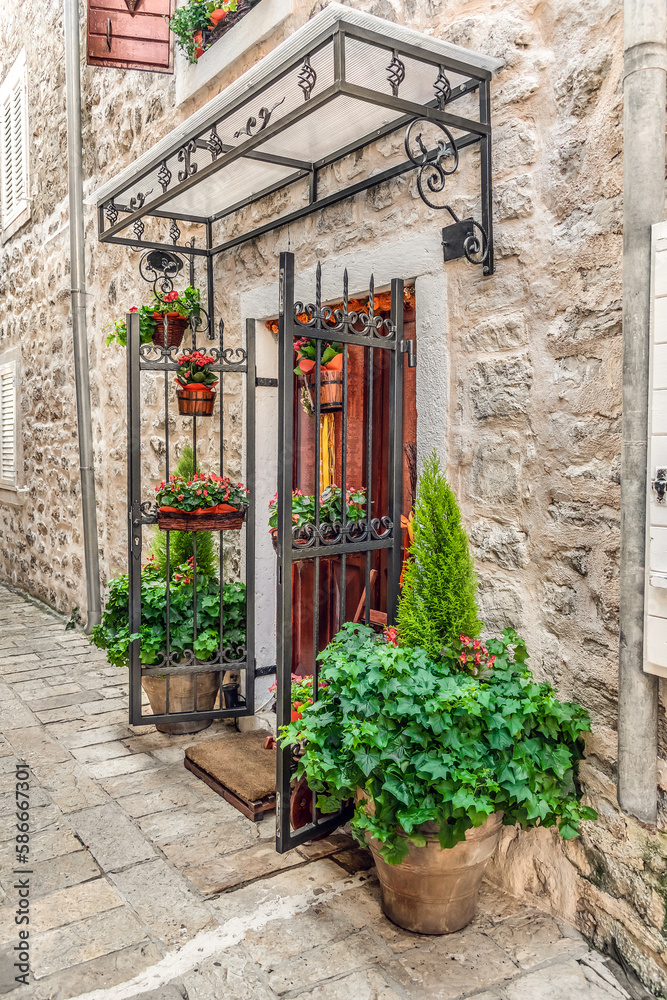 Flower vases decorate the entrance to an old stone building in the Old Town of Budva, Montenegro. Vertical view of flower pots at the door in Stari Grad