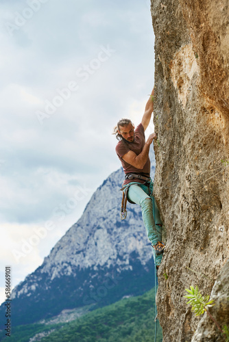 Rock climbing, outdoors activity with beautiful mountains view. Enthusiastic male climber on vertical rock with rope, lead climbing