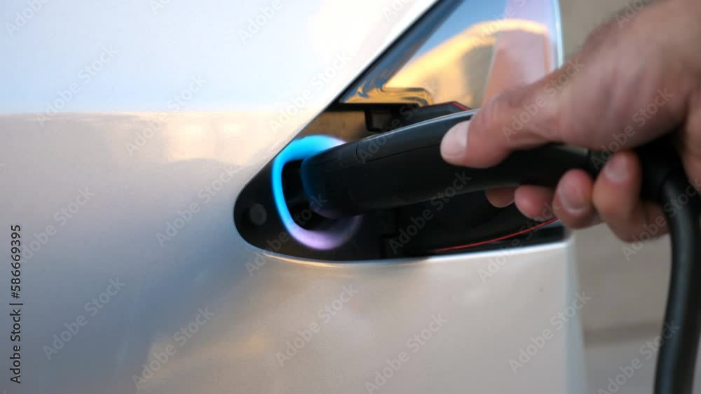 Hand opening an electric car charging socket cap and plugging in a