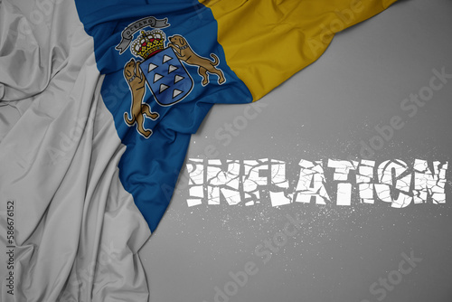 waving colorful national flag of canary islands on a gray background with broken text inflation. 3d illustration