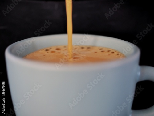 close up de una taza de café expresso que se está rellenando sobre fondo negro