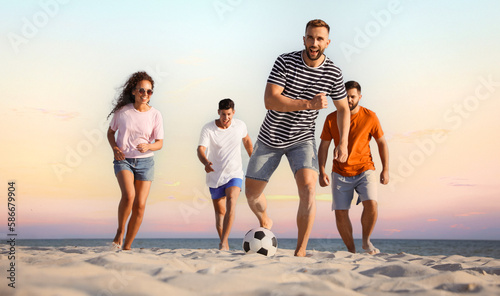 Fototapeta Naklejka Na Ścianę i Meble -  Happy friends playing football on beach during sunset, low angle view