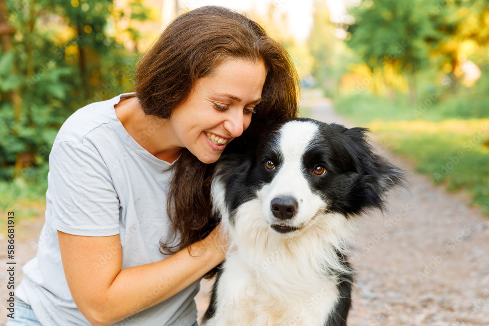 Smiling young attractive woman playing with cute puppy dog border collie on summer outdoor background. Girl holding embracing hugging dog friend. Pet care and animals concept Smiling young attractive woman playing with cute puppy dog border collie on summer outdoor background. Girl holding embracing hugging dog friend. Pet care and animals concept