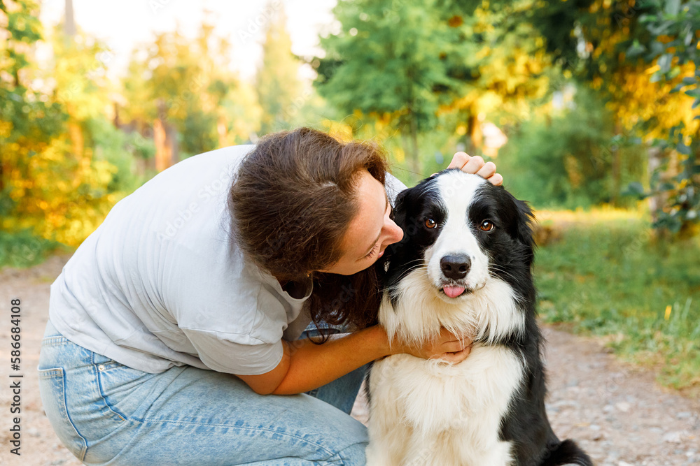 Young attractive woman playing with cute puppy dog border collie on summer outdoor background. Girl kissing holding embracing hugging dog friend. Pet care and animals concept