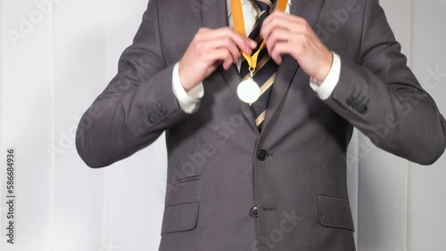 Man in classical suit puts on golden medal on yellow ribbon, rejoicing over victory, first place, achiving success in business, winning competition. Close up, 4K Ultra HD.