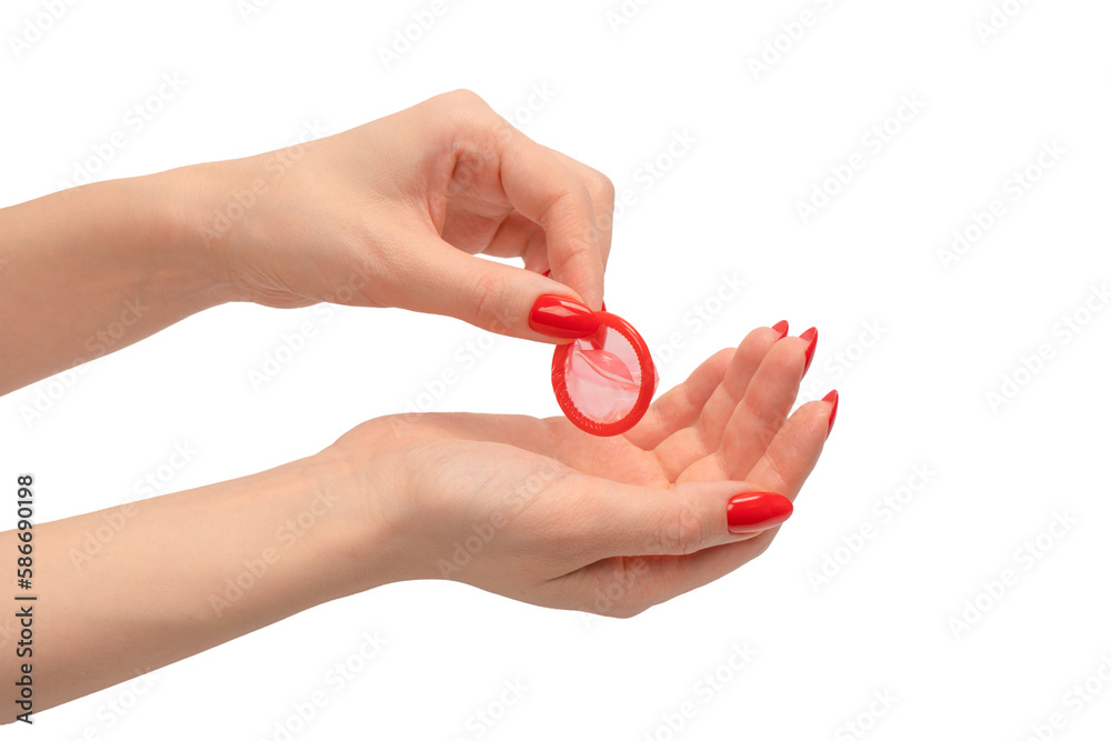 A red condom in a woman hand with red nails isolated on white background. A red condom in a woman hand with red nails isolated on white background.